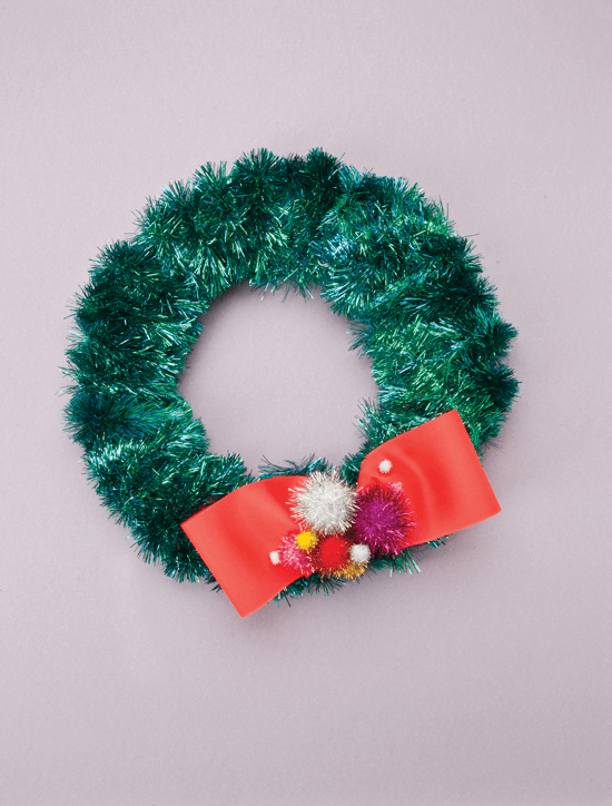 Holiday wreath wrapped in iridescent green garland finished off with a red bow and flashy pom-poms.