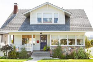 A white home with a blue door and neat lawn and landscaping.