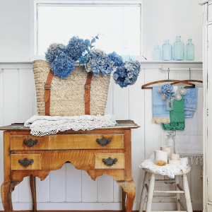 Antique wooden desk displaying a large straw purse filled with lavender hydrangeas.