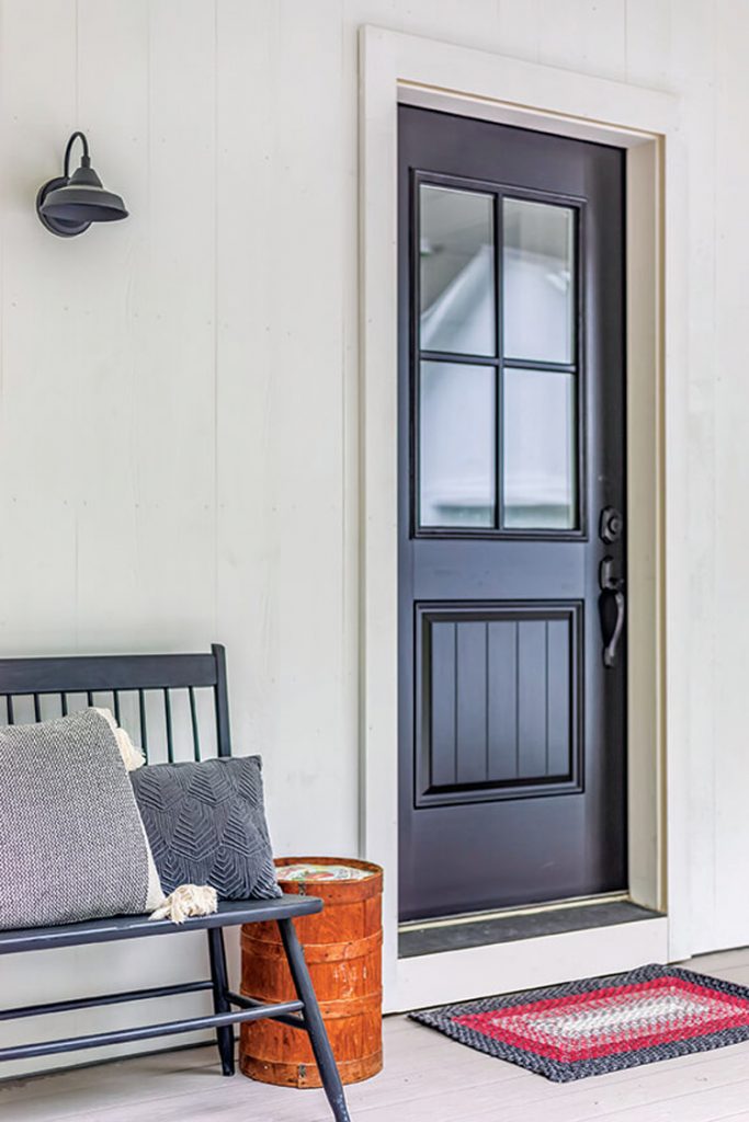 The exterior view of this house's front black door and bench shows how beautiful white painted siding looks with accent colors.