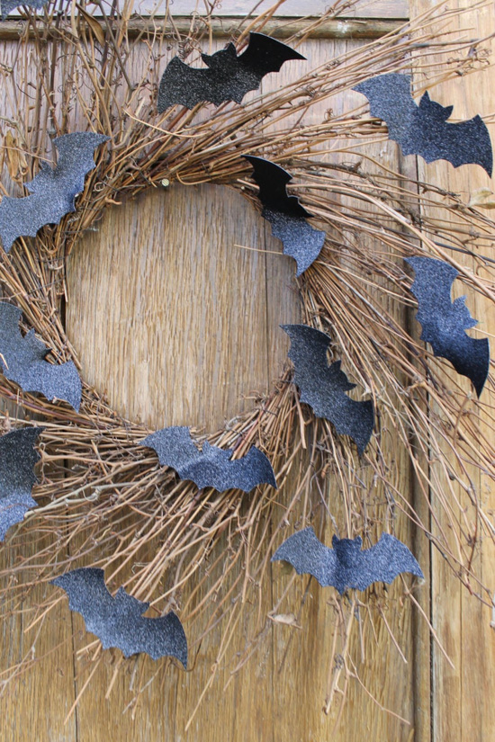 Natural burst wreath adorned with sparkly black bat cutouts hung on a wooden front door. 