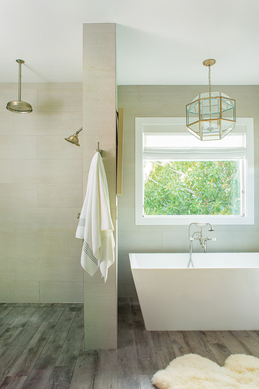 white bathroom with white tub, open shower, window with green tree in view 