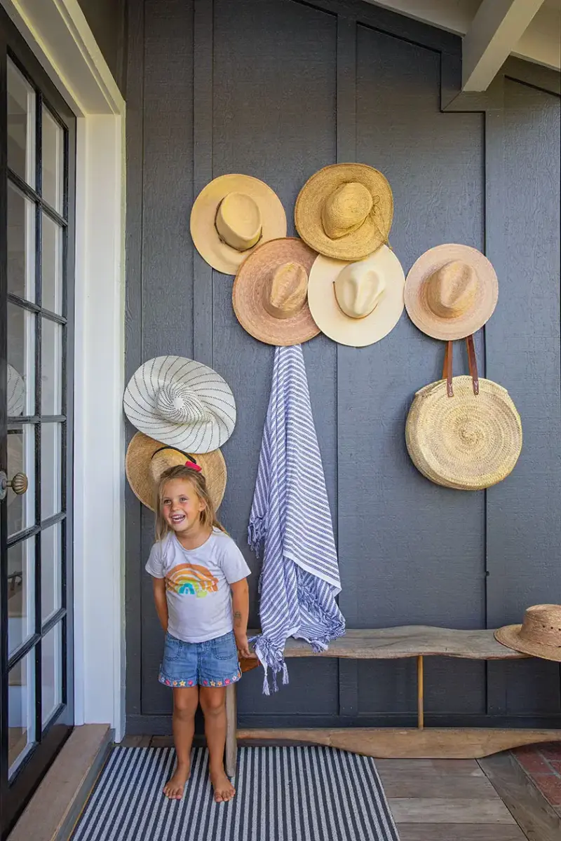 homeowner's daughter in entry way of beach cottage with hung beach hats on exterior wall behind her