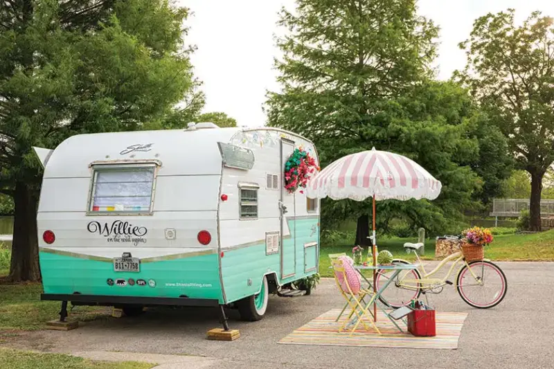 colorful camper with bright faux loral wreath and fringed pink shade umbrella and multi-colored bistro set