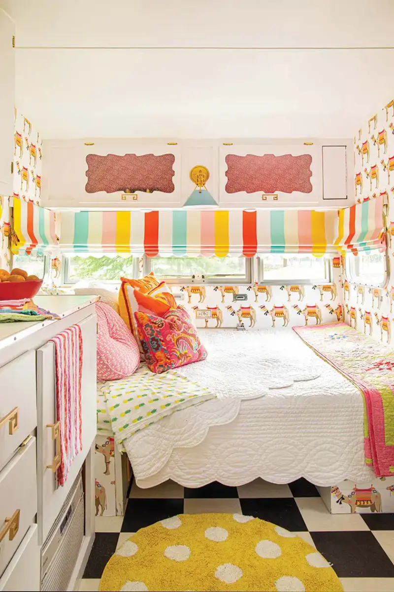 white coverlet and colorful throw pillows and stripped curtains inside colorful camper