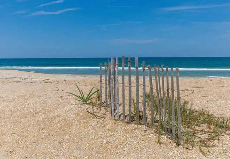 backyard of beachfront Florida home with simple partial fence for propping up a surfboard