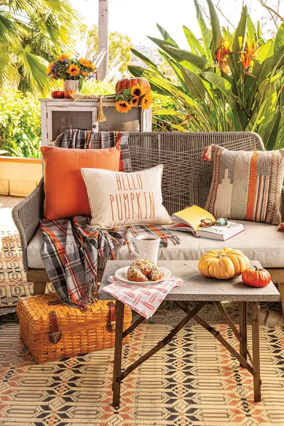 outdoor nook in California garden with cozy seating area with orange throw pillows and table with decorative pumpkins and almond croissant