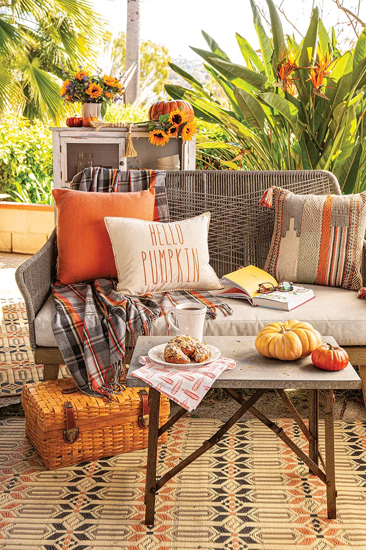 outdoor nook in California garden with cozy seating area with orange throw pillows and table with decorative pumpkins and almond croissant