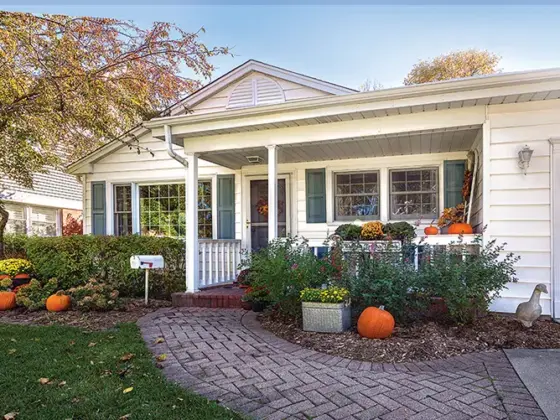 exterior of cozy cottage decorated for fall with front walkway decorated with several pumpkins and potted mums