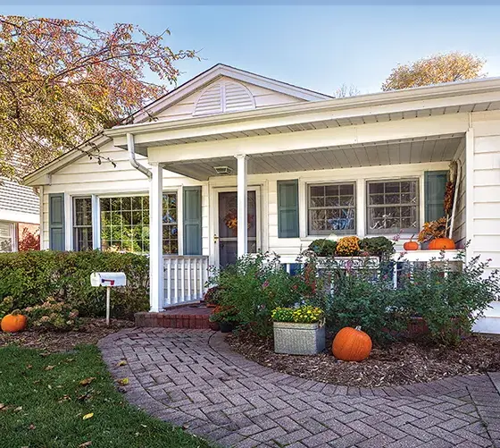 exterior of cozy cottage decorated for fall with front walkway decorated with several pumpkins and potted mums