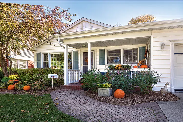 exterior of cozy cottage decorated for fall with front walkway decorated with several pumpkins and potted mums