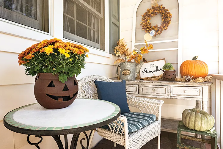 porch decorated for fall with Jack o Lantern plant pots containing mums and fall wreath