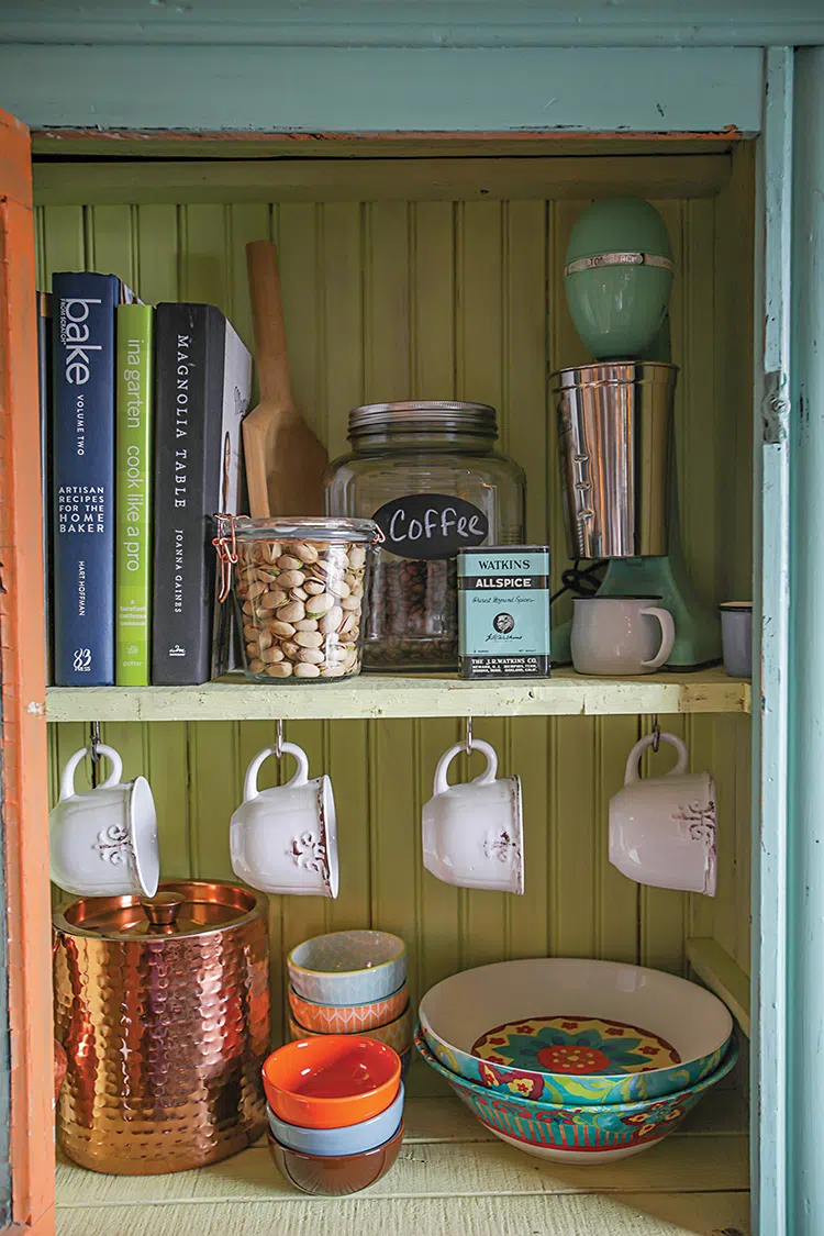 close up of hutch with turquoise exterior and lime green backing with milkshake maker, cookbooks, mugs and colorful bowls