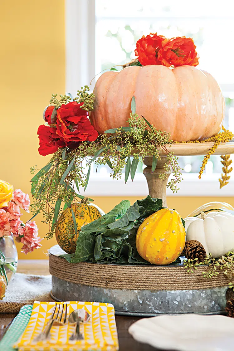 peach yellow and white colored pumpkins with large one on pedestal surrounded by leaves and flowers