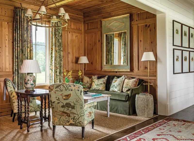 wood paneled walls surrounding window in sitting room with green furniture and duck patterned upholstery on side chairs and throw pillows