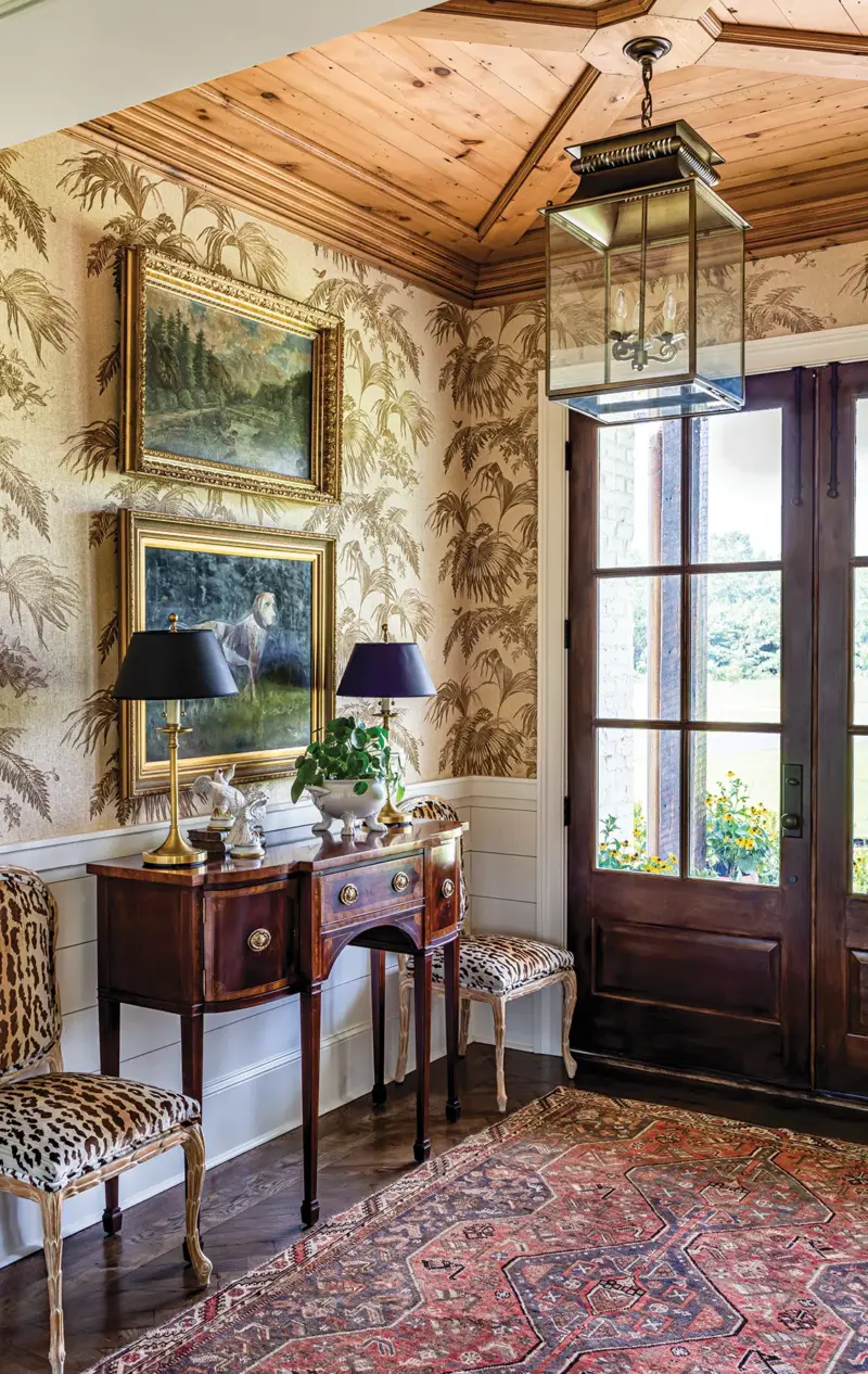 entryway with palm frond patterned wallpaper, animal print upholstery on side chairs and antique dresser