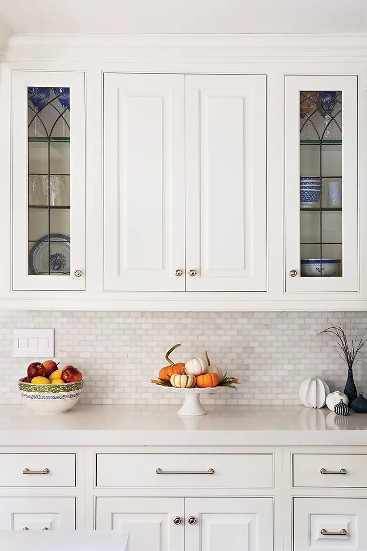 white quartz countertops, white cabinetry with traditional glass doors on outer cabinets in traditional kitchen decorated for fall with decorative pumpkins