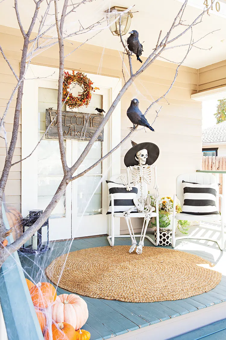 close up of porch with skeleton wearing witches hat and fake crows in branches