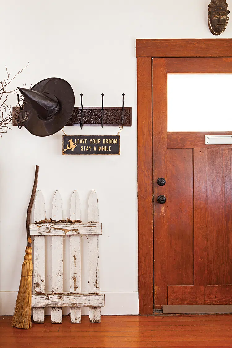 witches hat and broom propped up in entryway of home decorated for Halloween