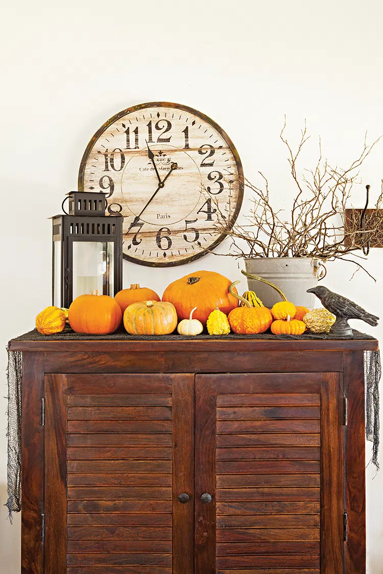 vignette of various sized pumpkins, bucket of twisted branches and crow figurine