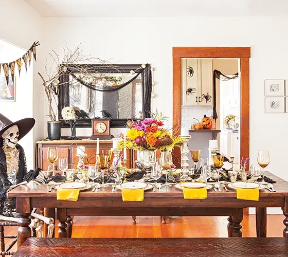 spooky and sophisticated Halloween dinner party tablescape with skeleton wearing black detailed shawl and witches hat