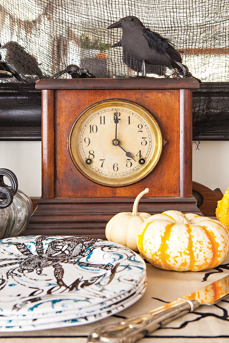 fake crow on top of vintage clock guarding stack of plates with spider design