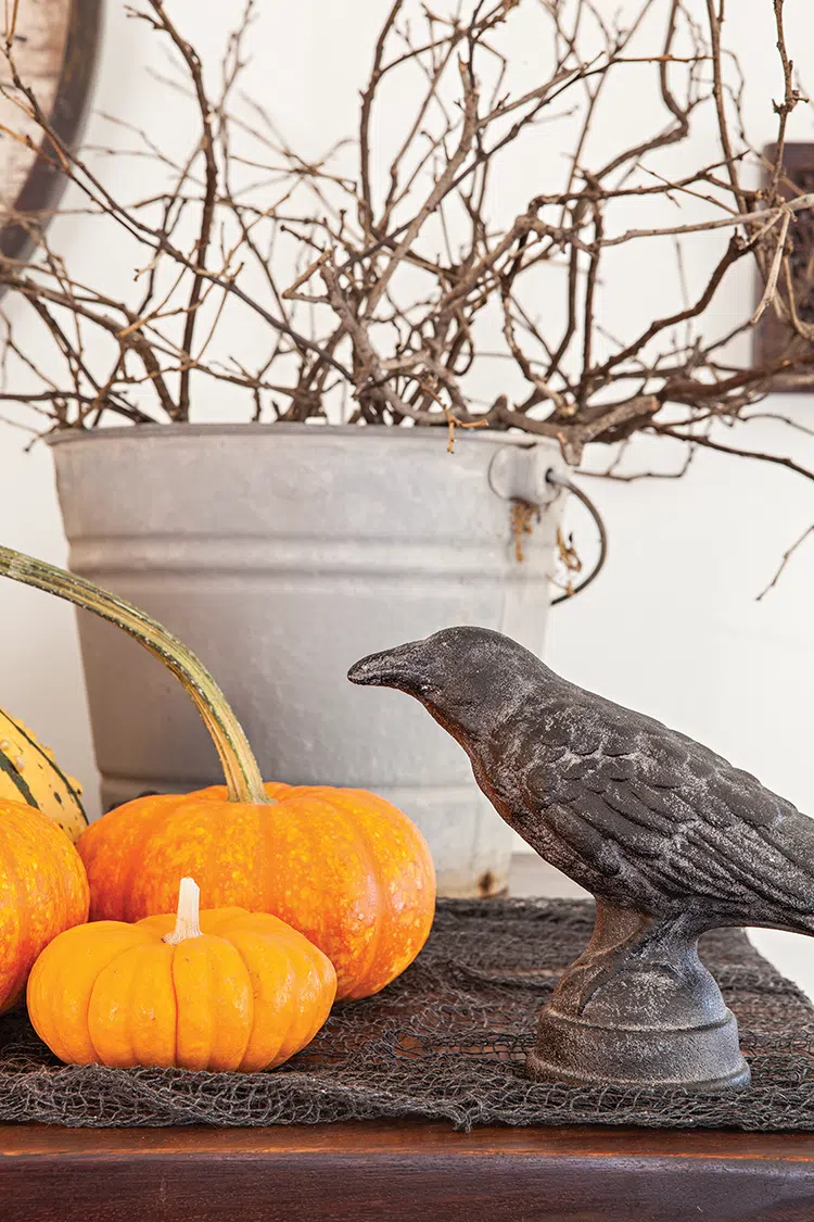 small pumpkins with crows figurine and bucket of twisted branches