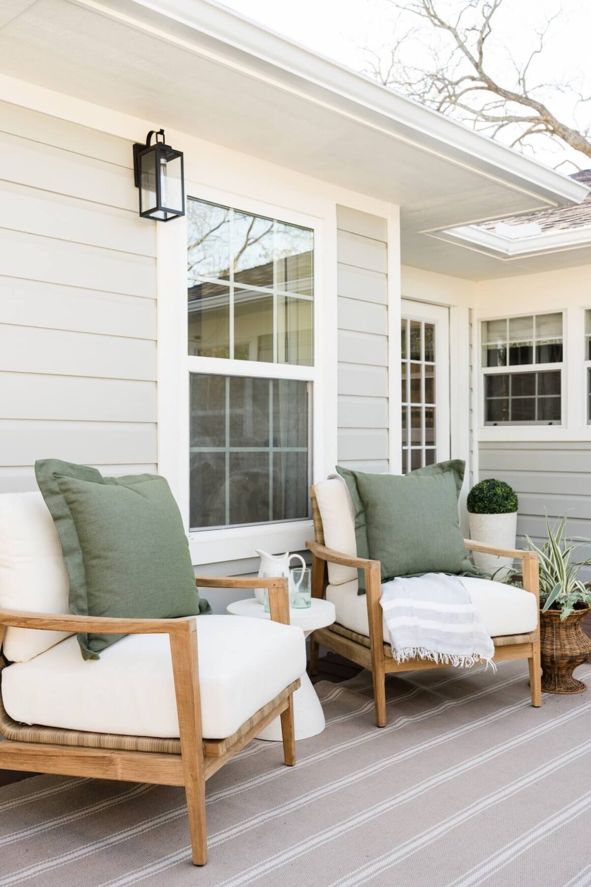 porch with wooden chairs woven planter and sage green throw pillows