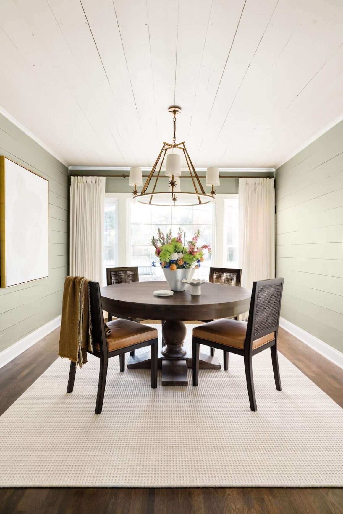 dining room with soft green shiplap walls and round dark wood dining table