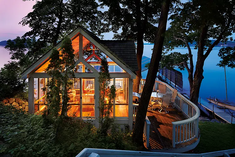 warm light emanating from lakeside home with floor to ceiling windows