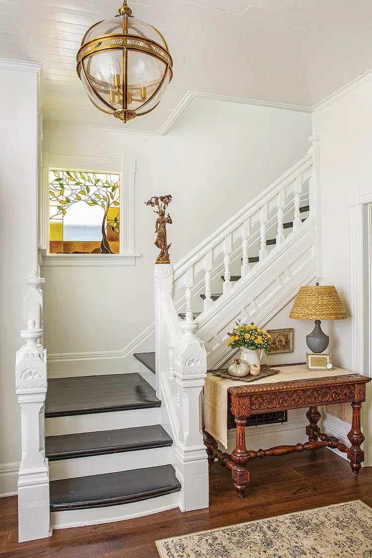 stairway in Victorian home with stained glass window and antique table decorated with vintage finds and fall flowers and pumpkins