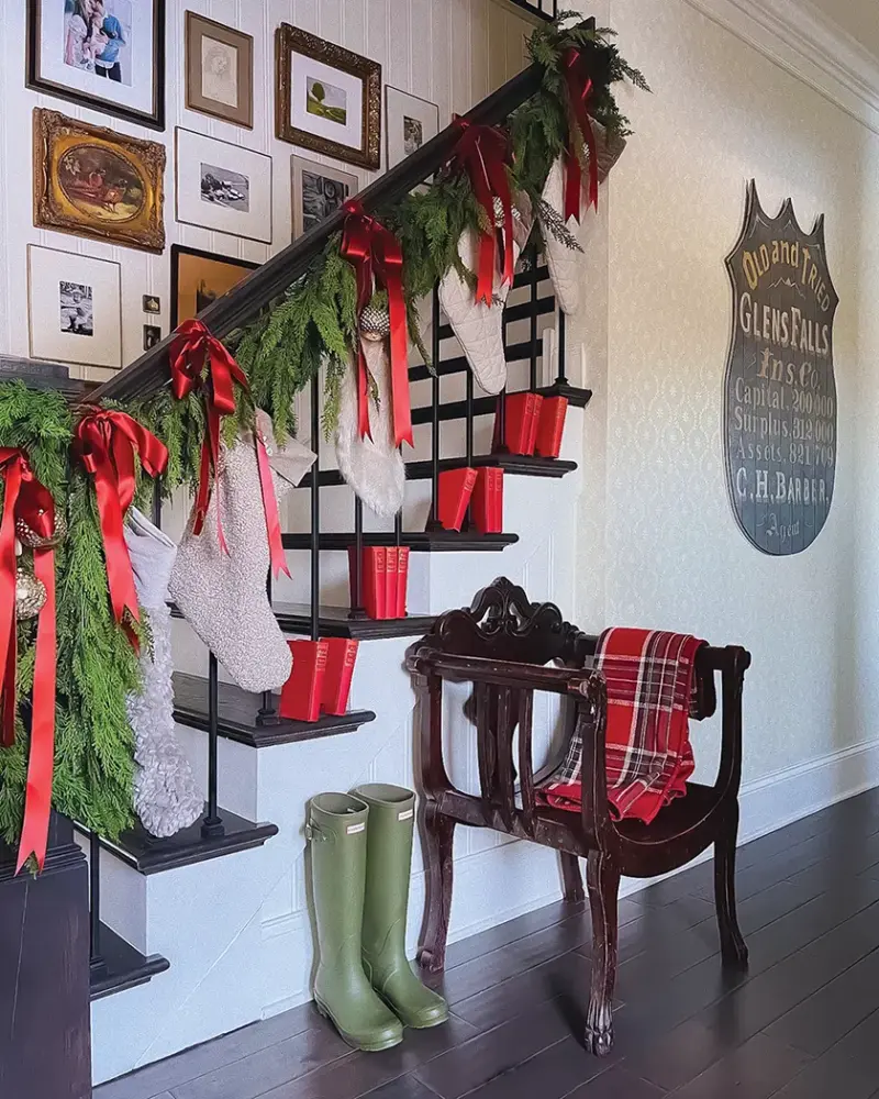 gallery wall along staircase with bannister decorated with natural garland and red ribbon