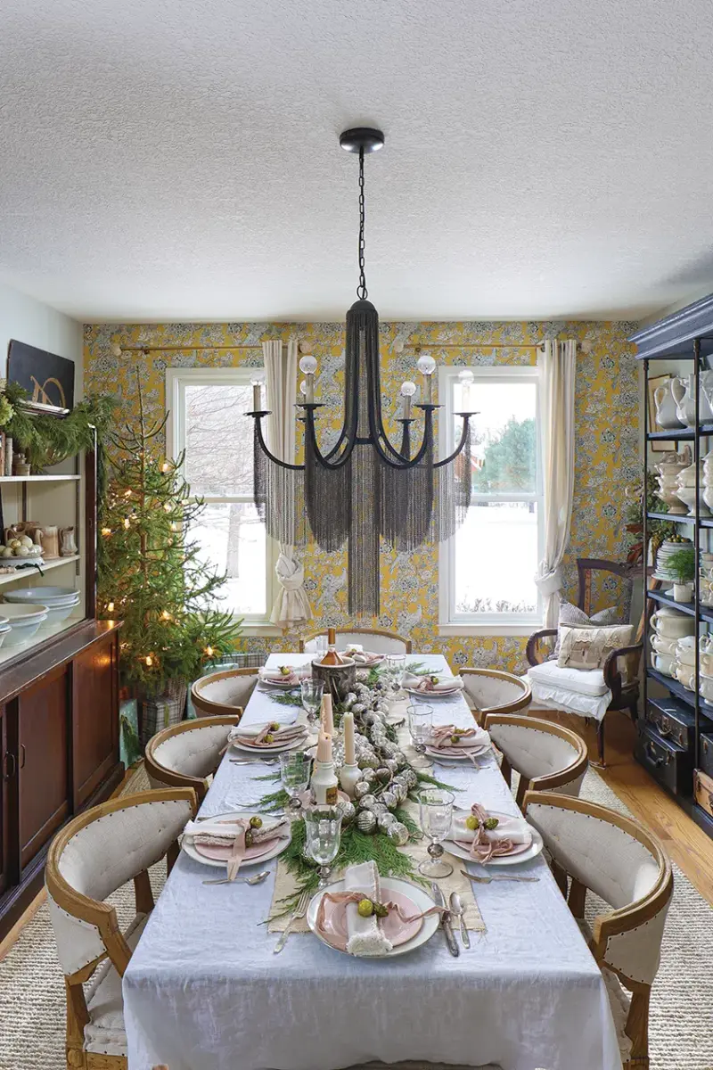 dining room with fringed chandelier and table runner decorated with natural greenery