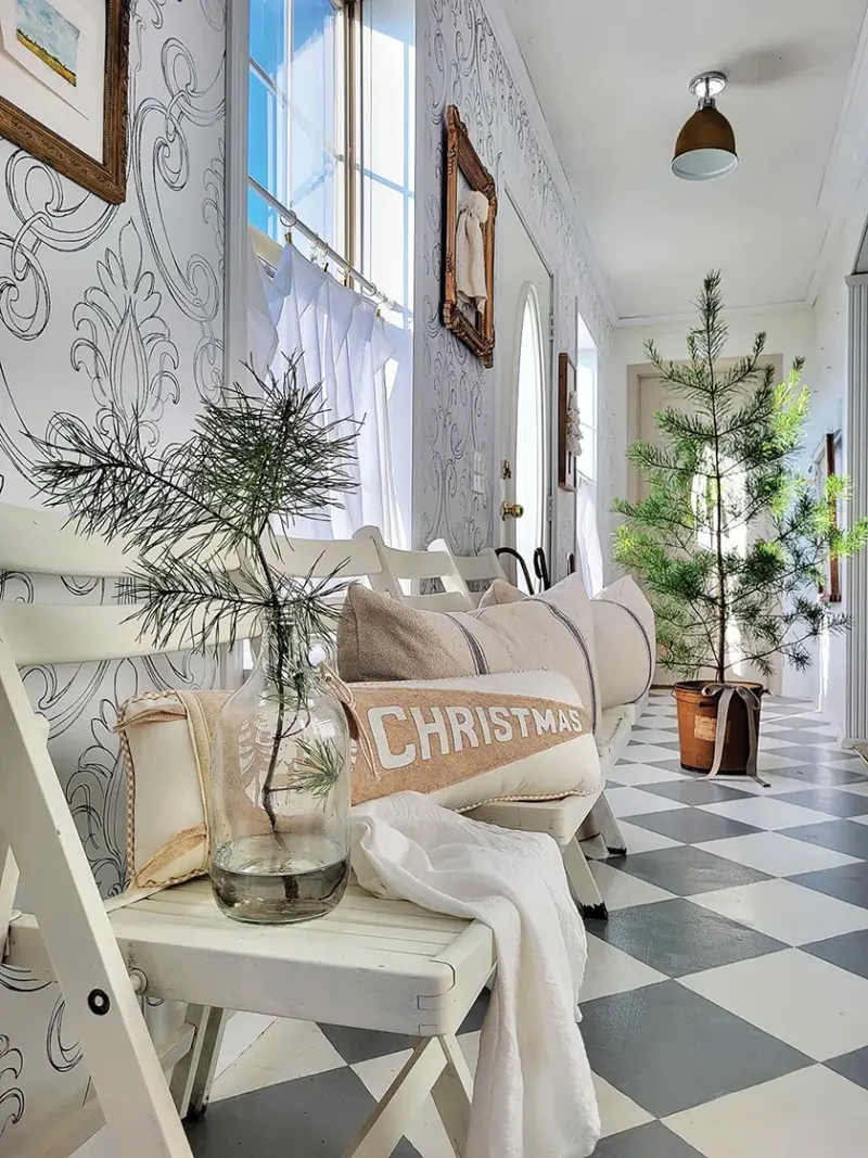 Christmas tree in entryway of neutral cottage with jar featuring a pine branch on entryway chair