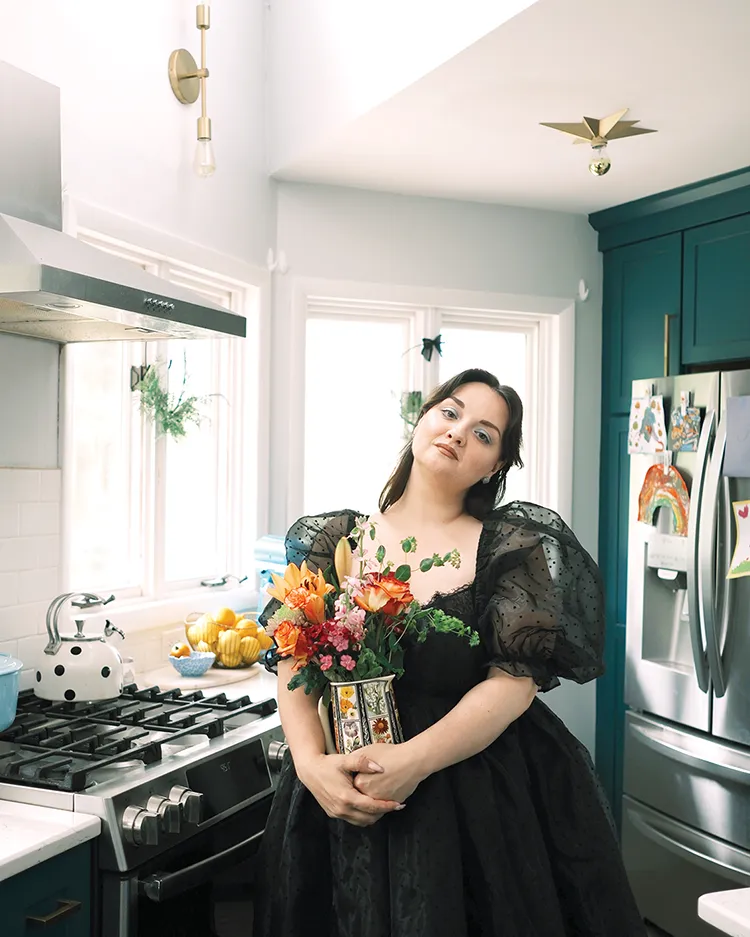 fridge stylist holding vase of flowers in her kitchen