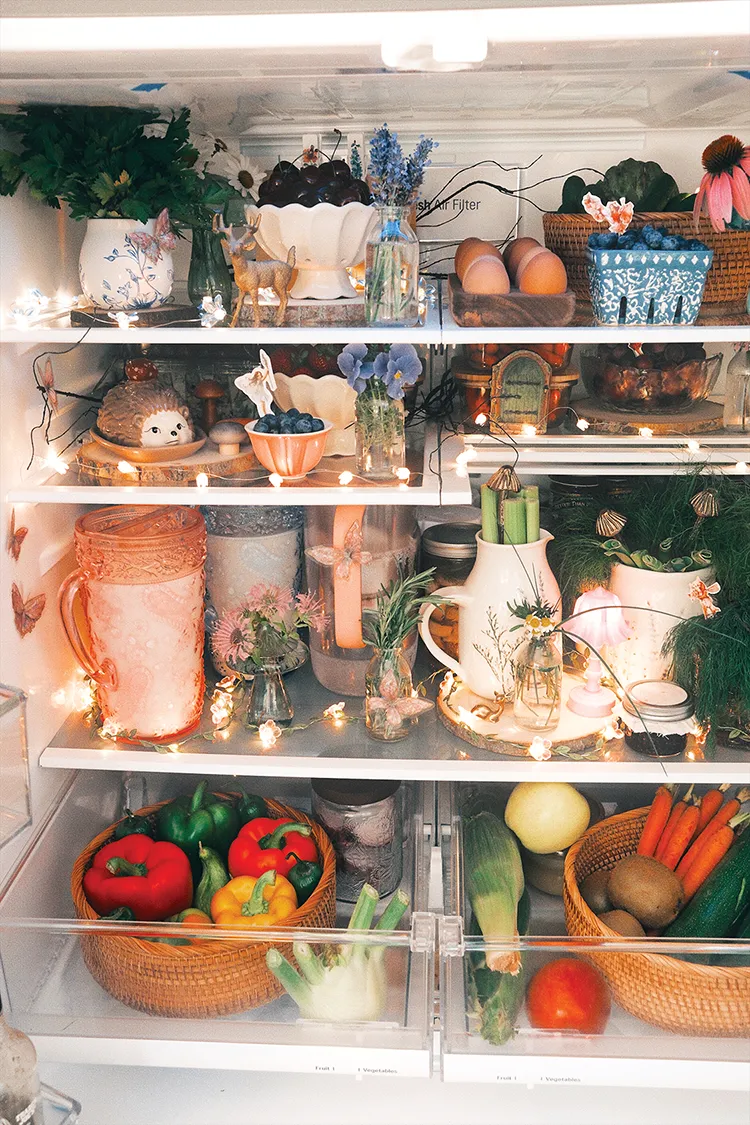 styled refrigerator with fairy lights small figurines and vases of flowers around well organized baskets and ceramic food storage