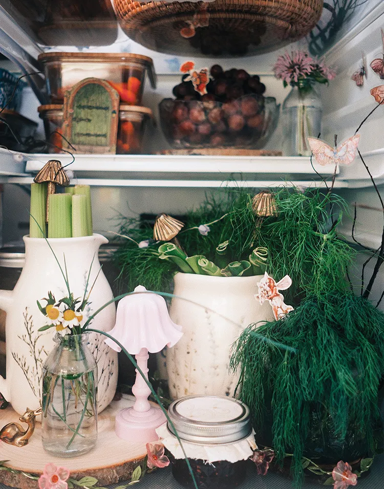 vignetter with fruits and veggies in cute bowls pitchers and containers along with floral lights in styled refrigerator