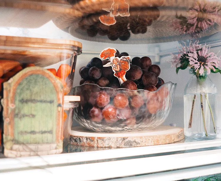 grapes in clear bowl next to small vase of flowers inside refrigerator