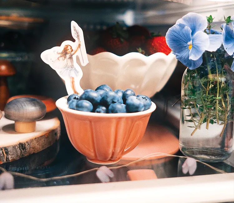 bowls of fruit and vase of blue pansies inside refrigerator