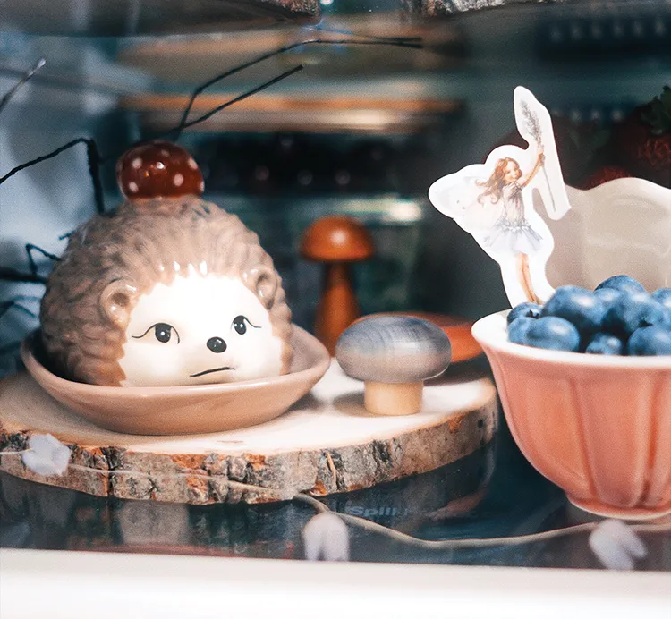 ceramic hedgehog vignette next to bowl of blueberries in styled refrigerator