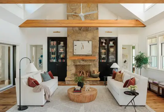 living room with natural stone fireplace and black glassfront bookshelves in otherwise white room