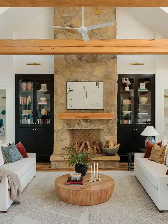 living room with natural stone fireplace and black glassfront bookshelves in otherwise white room